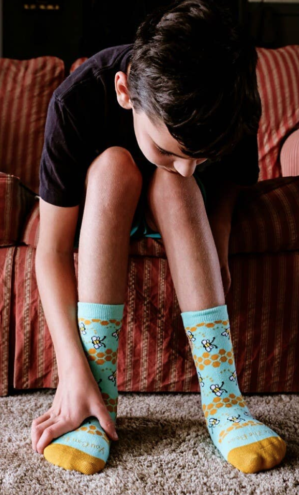 Boy bends down to touch his sockietalkies in a bee design